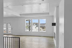 Unfurnished living room featuring light wood-type flooring, a raised ceiling, and a textured ceiling