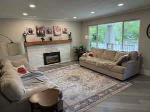 Living area featuring wood finished floors, ornamental molding, recessed lighting, a textured ceiling, and a brick fireplace