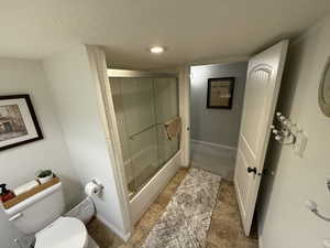 Bathroom featuring toilet and bath / shower combo with glass door
