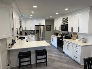 Kitchen featuring tasteful backsplash, stainless steel appliances, light stone countertops, white cabinets, and a peninsula
