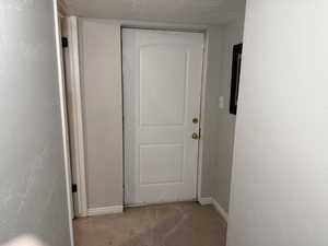 Hall with a textured ceiling, carpet flooring, and a textured wall
