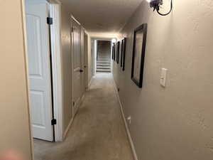 Hall with a textured ceiling, a textured wall, and light carpet