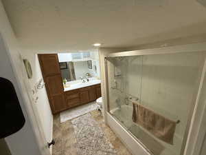 Bathroom featuring vanity, shower / bath combination with glass door, and a textured ceiling