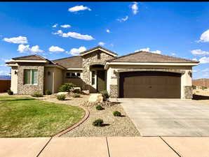 View of front of home with stucco siding, stone siding, driveway, and an attached garage