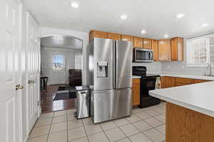 Kitchen with light countertops, stainless steel appliances, arched walkways, wood finish cabinetry, and recessed lighting