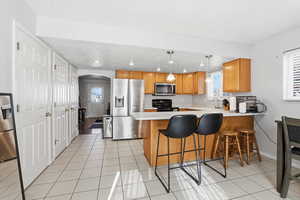 Kitchen with arched walkways, light countertops, a peninsula, stainless steel appliances, and a kitchen bar