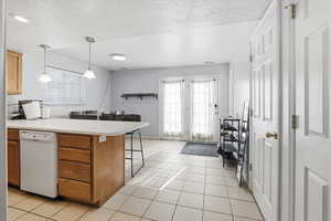 Kitchen featuring a peninsula, light countertops, a breakfast bar, dishwasher, and a textured ceiling