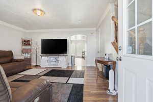 Living area featuring arched walkways, ornamental molding, wood finished floors, and a textured ceiling