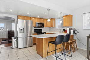 Kitchen featuring light countertops, stainless steel appliances, a peninsula, hanging light fixtures, and a breakfast bar area