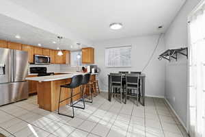 Kitchen featuring stainless steel appliances, hanging light fixtures, light countertops, a breakfast bar area, and a peninsula