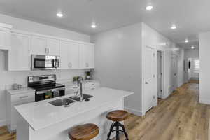 Kitchen featuring stainless steel appliances, a breakfast bar area, white cabinets, light wood-type flooring, and light stone countertops