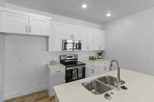 Kitchen featuring stainless steel appliances, white cabinetry, light wood-style floors, light stone countertops, and recessed lighting