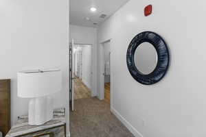 Corridor featuring light colored carpet and baseboards