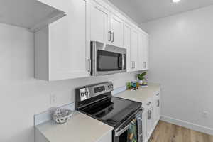 Kitchen with stainless steel appliances, white cabinetry, light wood-style flooring, and light stone counters