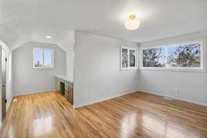 Bonus room with lofted ceiling, light wood-style flooring, and built in desk