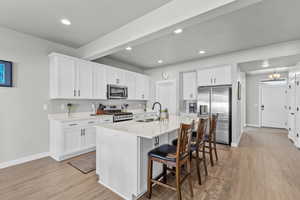 Kitchen with a kitchen bar, stainless steel appliances, white cabinets, and light wood finished floors