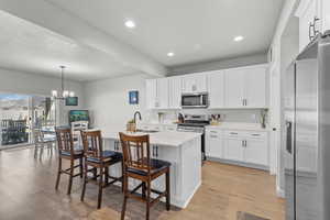Kitchen with a center island with sink, stainless steel appliances, white cabinetry, and beamed ceiling