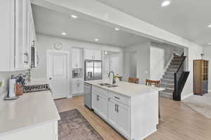 Kitchen featuring white cabinets, a kitchen island with sink, stainless steel appliances, light wood-style flooring, and light stone countertops