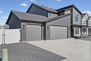 View of front of property featuring a gate, an attached garage, a shingled roof, and driveway