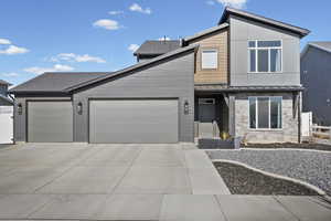 Contemporary home, an attached garage, concrete driveway, and stone siding