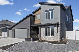 Contemporary home featuring stone siding, a garage, driveway, and a gate