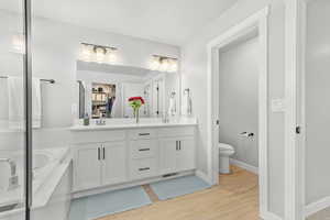 Full bath featuring double vanity, a bath, light wood finished floors, a shower with door, and a spacious closet