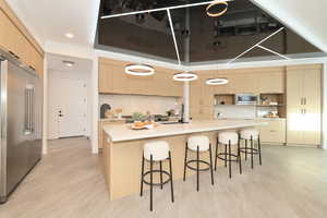 Kitchen with light wood finish cabinets, a kitchen bar, built in appliances, a large island, and pendant lighting