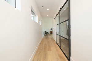 Corridor with a barn door, light wood-type flooring, and recessed lighting