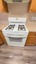 Kitchen view of wood finish cabinets, white range with gas cooktop, and light countertops