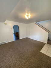 Empty room featuring carpet flooring, arched walkways, and suspended lighting