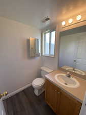 Half bathroom with vanity, dark wood finished floors, and a textured ceiling