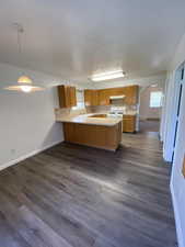 Kitchen with light countertops, a peninsula, white gas range, and dark wood-style flooring
