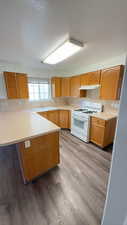 Kitchen with light countertops, white range with gas cooktop, a peninsula, light wood finished floors, and a breakfast bar area
