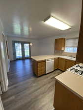 Kitchen featuring light countertops, wood finish cabinets, a peninsula, dishwasher, and dark wood-style flooring