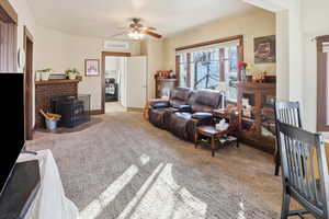 Living room featuring light carpet, ceiling fan, and a wood stove