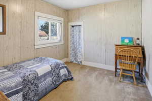 Bedroom with light colored carpet and wooden walls