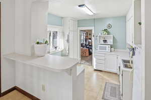 Kitchen featuring white cabinets, light countertops, white appliances, and a peninsula