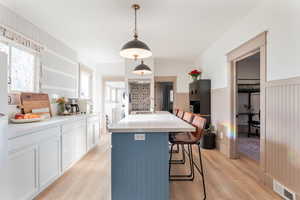 Dual tone kitchen featuring a breakfast bar, an island with sink, light wood-style flooring, wainscoting, and decorative light fixtures