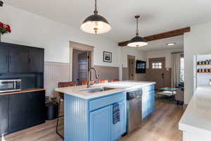 Kitchen featuring a breakfast bar, an island with sink, light wood-style floors, blue cabinets, and decorative light fixtures
