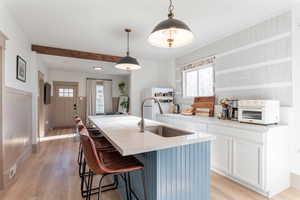 Dual tone kitchen featuring a breakfast bar area, decorative light fixtures, light wood finished floors, a kitchen island with sink, and healthy amount of natural light