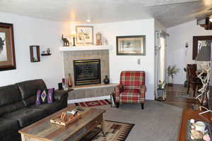 Living room with a fireplace, dark carpet, and vaulted ceiling
