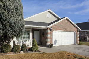 Ranch-style home with brick siding, a shingled roof, concrete driveway, a garage, and covered porch