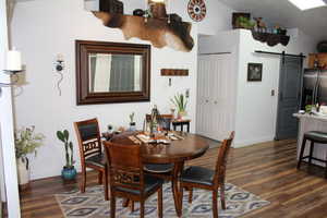 Dining room with a barn door, dark wood-type flooring, and lofted ceiling