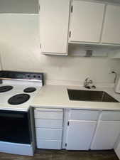 Kitchen featuring white electric stove, dark wood-type flooring, and white cabinetry
