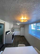Kitchen featuring white appliances, light countertops, white cabinets, dark wood-style floors, and a textured ceiling