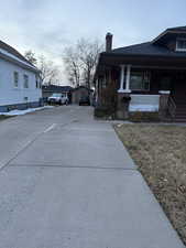 View of home's exterior with a porch, a chimney, driveway, and a yard