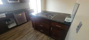 Kitchen with stainless steel appliances, dark stone countertops, dark wood-type flooring, and dark wood finish cabinets