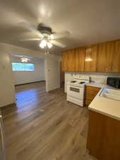 Kitchen with wood finish cabinetry, white electric stove, light countertops, dark wood-type flooring, and black microwave
