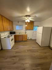 Kitchen with wood finish cabinetry, white appliances, light countertops, and dark wood-style flooring