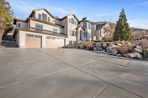 View of front of house featuring a standing seam roof, driveway, an attached garage, stucco siding, and stone siding